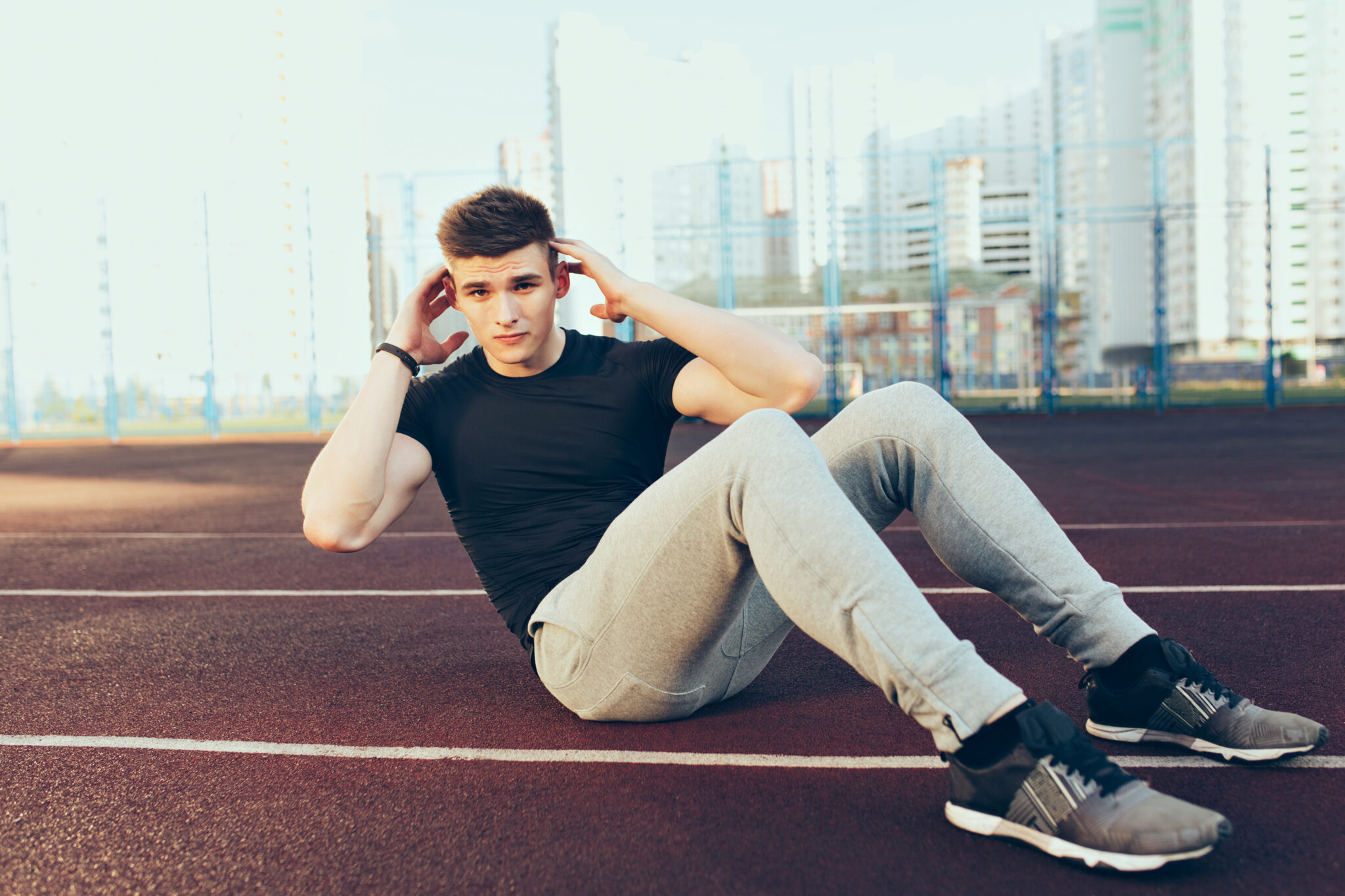 Strong guy with a good body training in the morning on stadium. He wears sport clothes, rocks press. He looks to the camera.